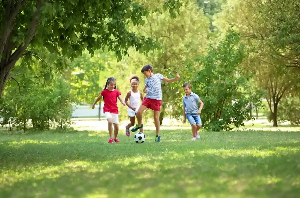 Group of diverse children playing soccer safely on a green lawn after mosquito treatment.