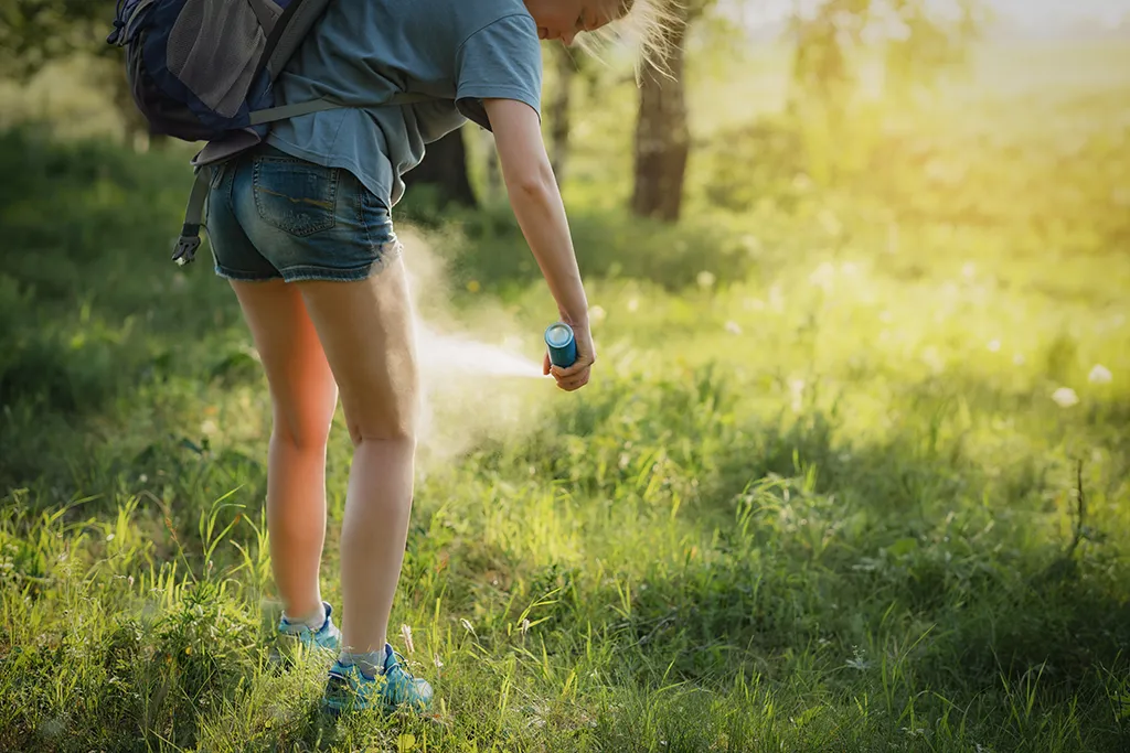 Person in tall grass applying mosquito spray to their legs