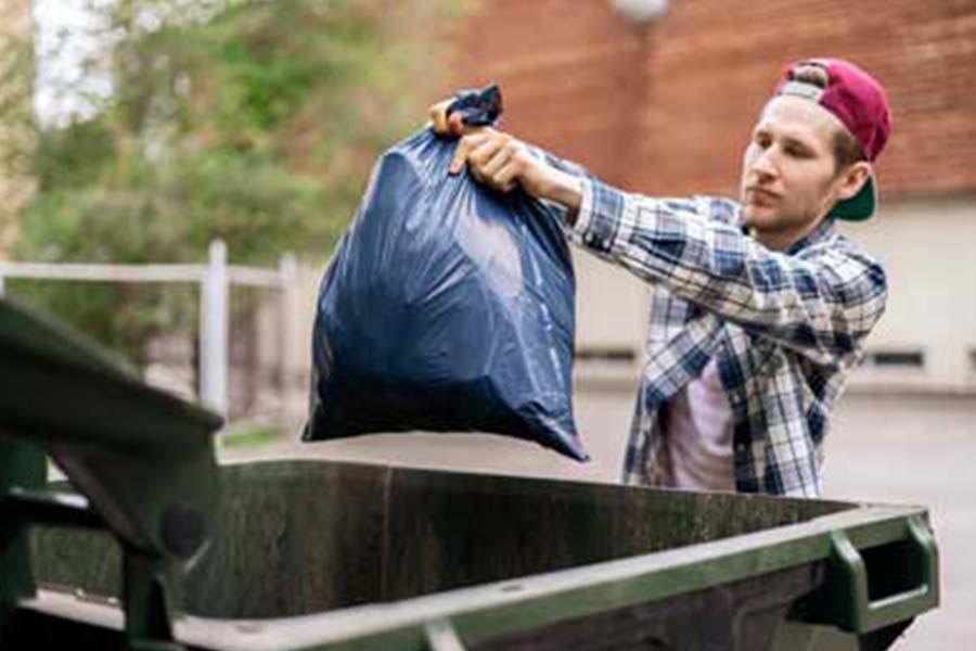 Man throwing garbage bag into dumpster