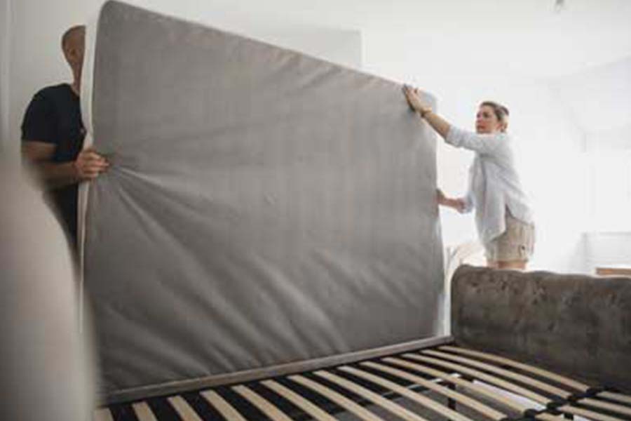 Two people lifting mattress off of bed frame