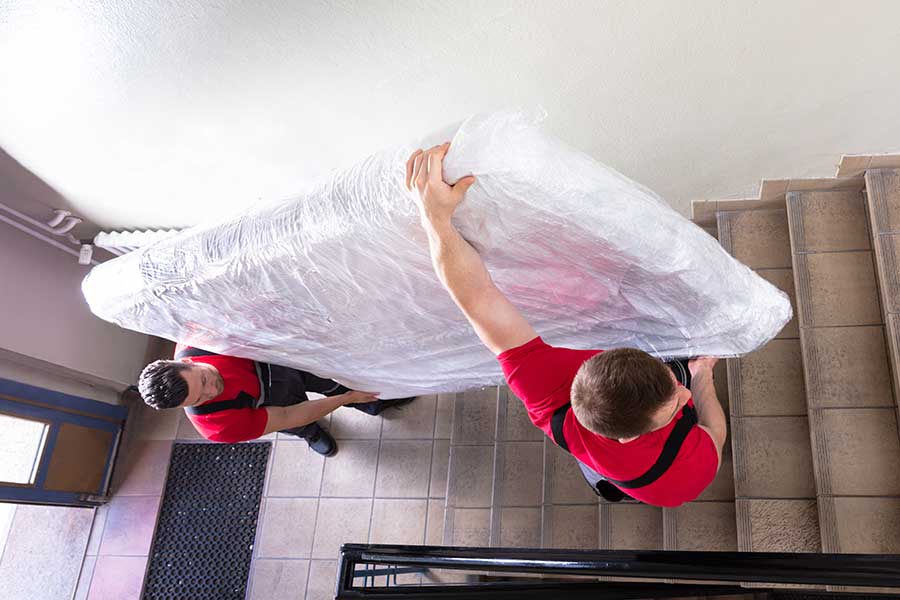 Two men carrying mattress up stairs