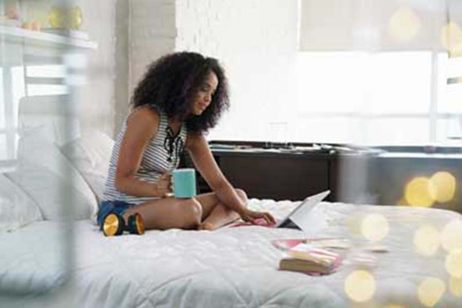 Woman on bed with drink and laptop