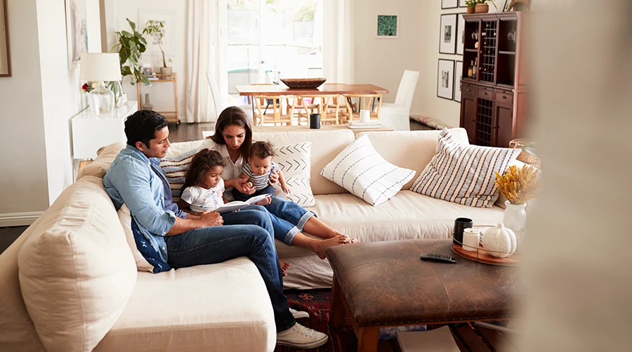 Family sitting on a white couch in the living room of their home reading a book to their children